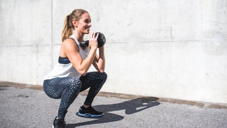 Eine Frau trainiert draußen mit einer Kettlebell.