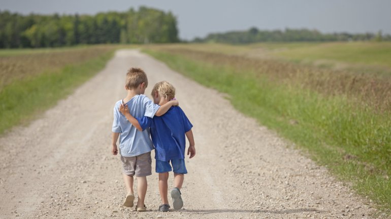 Man sieht zwei Jungen von hinten, die Arm in Arm gehen.