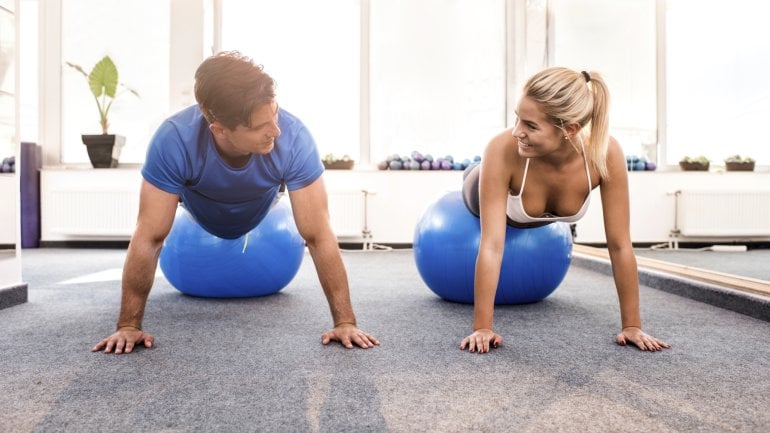 Ein Mann und eine Frau machen Liegestütz mit einem Gymnastikball.