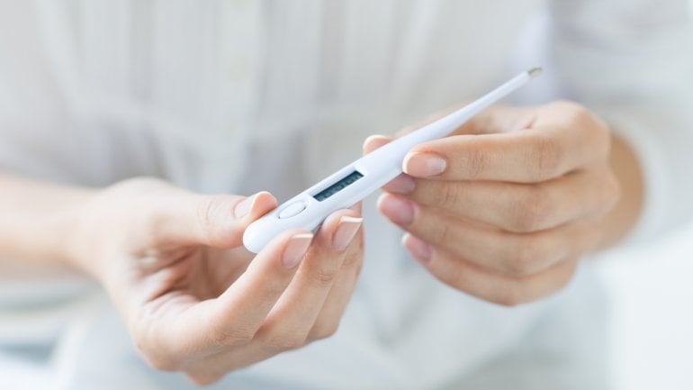 Frau hält ein Fieberthermometer in der Hand.