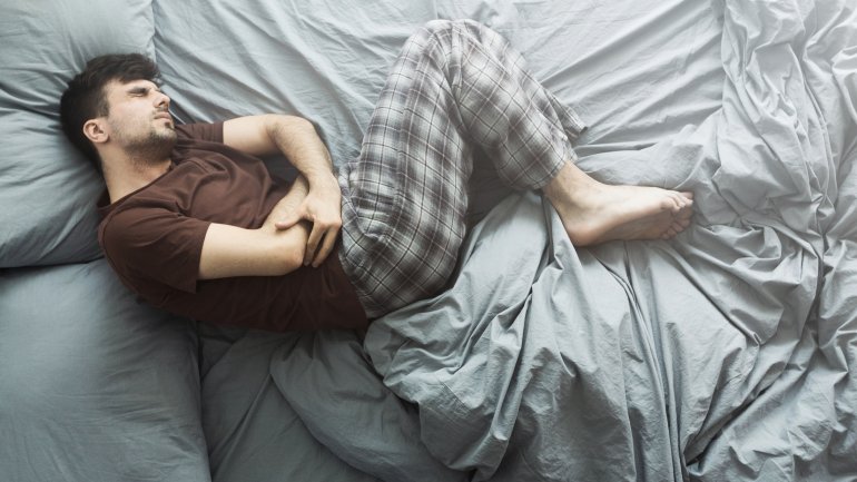 Ein Mann liegt mit starken Bauchschmerzen im Bett und hat eine Schonhaltung mit angezogenen Beinen eingenommen.