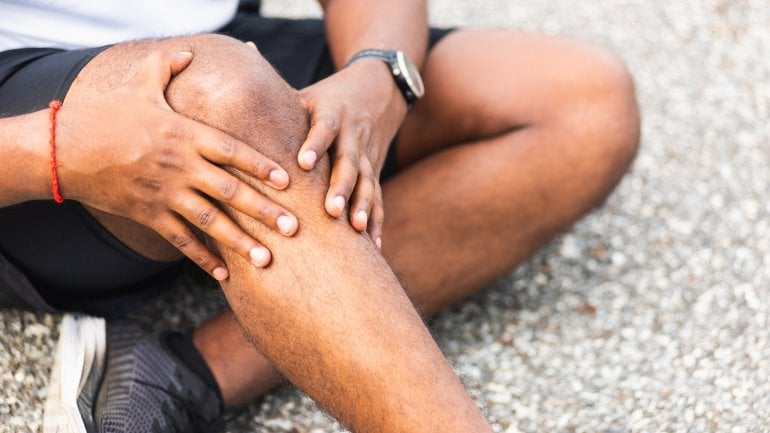 Mann sitzt auf Boden, fasst sich an Knie und leidet unter einem Kreuzbandriss