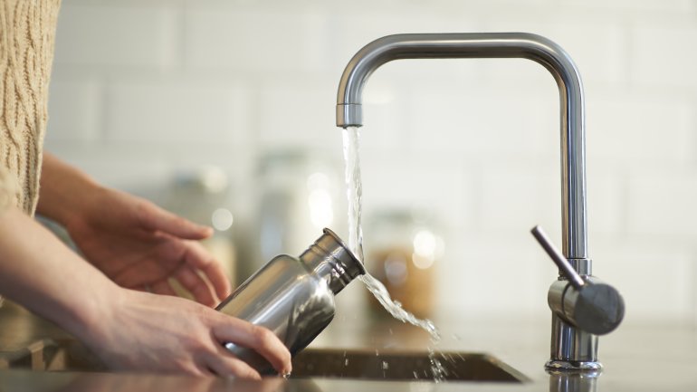 Eine Person füllt eine Trinkflasche am Wasserhahn mit Trinkwasser.