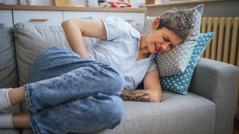 Frau mit Magengeschwür liegt mit Schmerzen im Bauch auf dem Sofa.