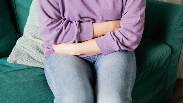 Frau mit Magenkrebs sitzt auf Sofa und hält sich den schmerzenden Bauch.