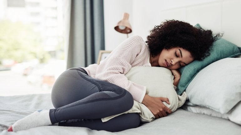 Eine Frau mit Bauchschmerzen liegt im Bett.