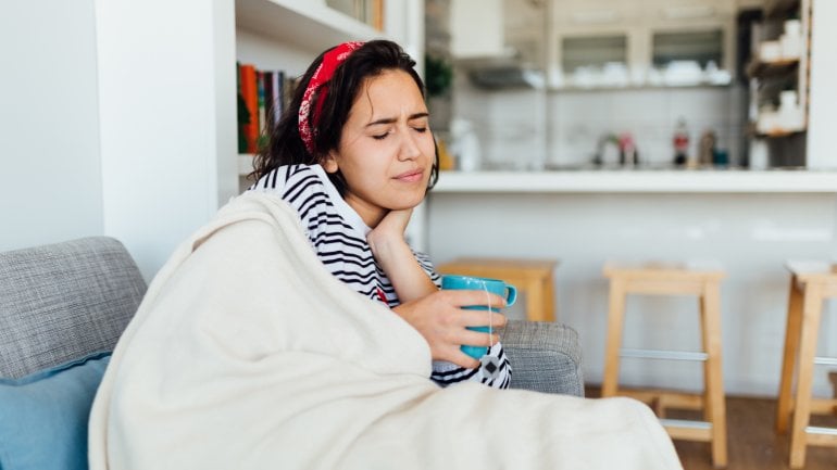 Frau mit Mandelentzündung sitzt auf dem Sofa und hat Halsschmerzen.