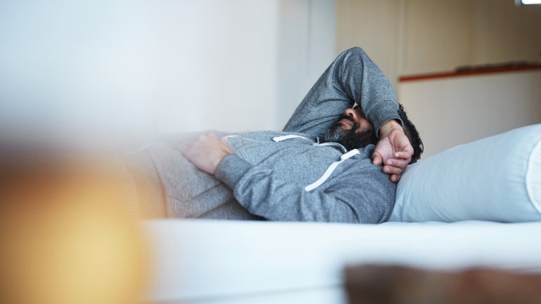 Ein Mann liegt auf dem Bett und hat einen Arm über die Augen gelegt.