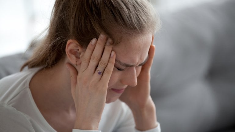 Junge Frau mit Meningitis fasst sich an schmerzenden Kopf.