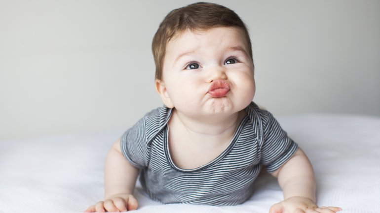 Ein Baby liegt auf dem Bauch, stützt sich ab und zieht eine Schnute