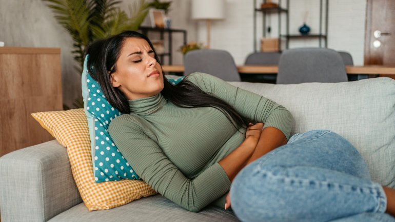 Frau mit Morbus Crohn liegt mit Bauchschmerzen auf dem Sofa.