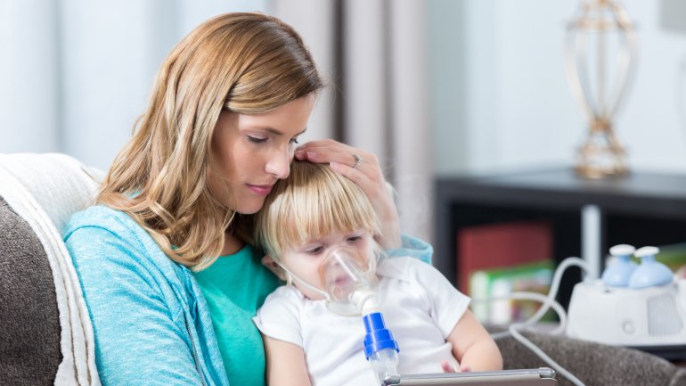 Kind mit Mukoviszidose inhaliert auf dem Schoß der Mutter.