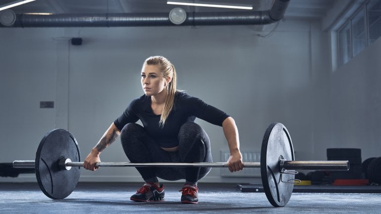 Eine Frau im Fitnessstudio mit einer Langhantel.