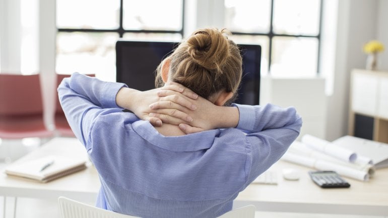 Eine Frau sitzt am PC und verschränkt die Hände im Nacken.