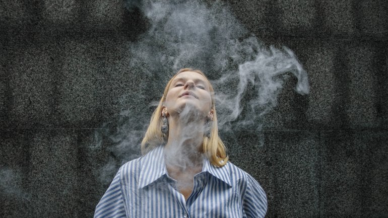 eine junge Frau bläst Rauch von einer Zigarette aus