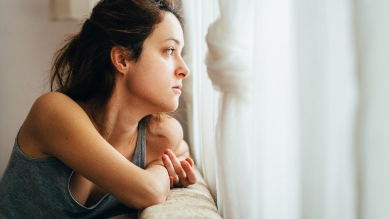 Eine Frau schaut betrübt und ängstlich aus dem Fenster.