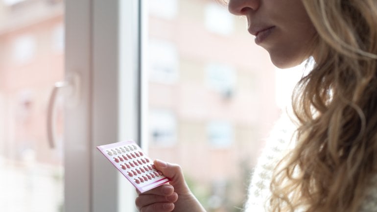 Eine Frau steht am Fenster und hält eine Pillenpackung in der Hand.