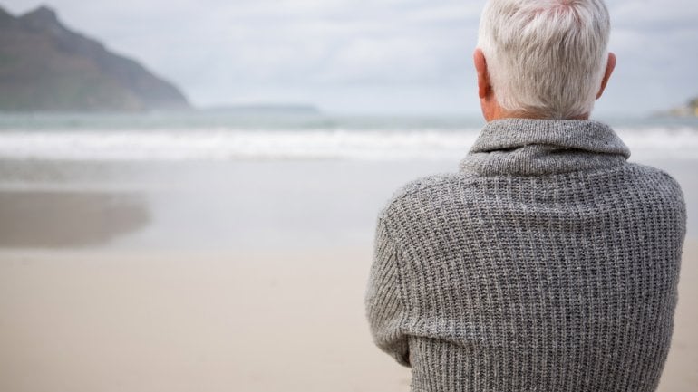 Ein älterer Mann steht am Strand und schaut aufs Meer.