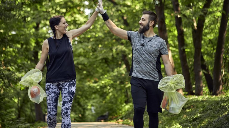 Man sieht einen Mann und eine Frau beim Plogging im Wald.