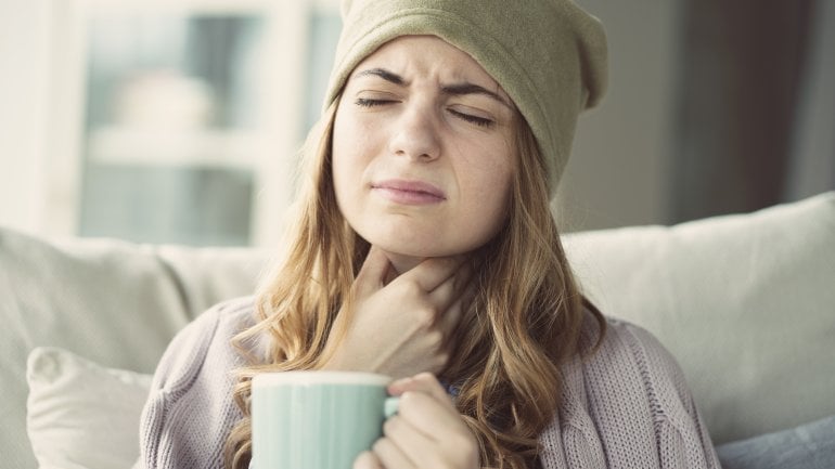 Frau hält eine Tasse in der Hand und fasst sich an den Hals.