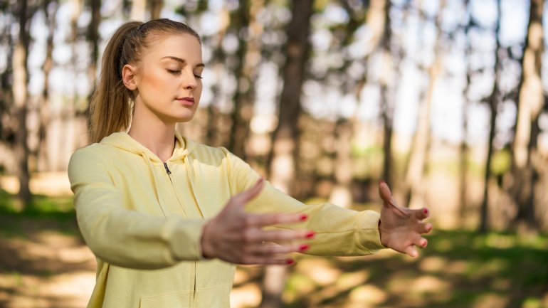 Qigong: Junge Frau führt in der Natur Übungen durch.