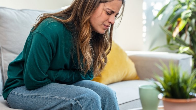 Frau sitzt auf Sofa und leidet unter starken Regelschmerzen.