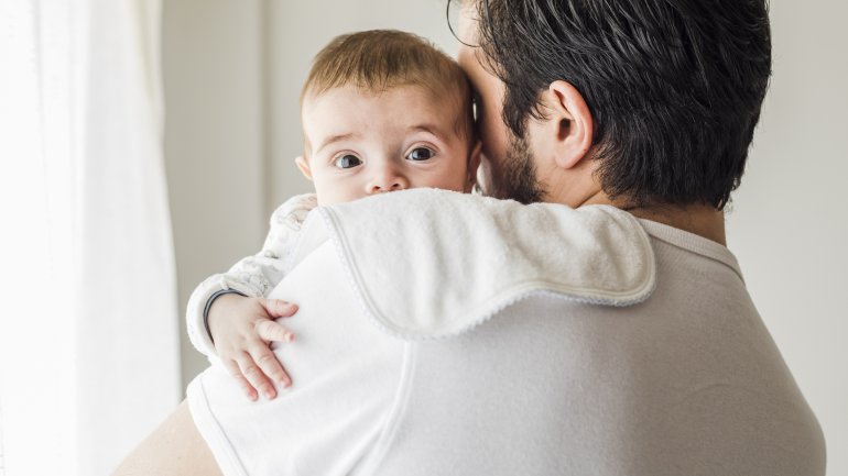 Man sieht ein Baby über der Schulter seines Vaters hervorschauen