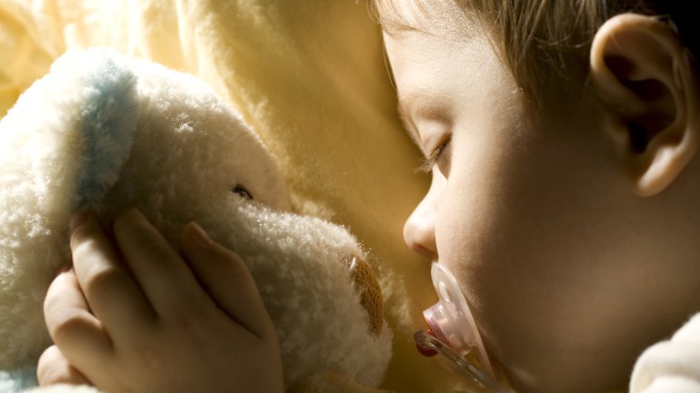 Baby schläft mit Schnuller und Teddy.