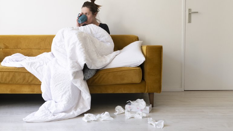 Eine Frau sitzt mit Decke und Tee auf dem Sofa