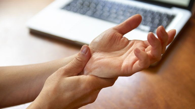 Bild einer Person mit Sehnenscheidenentzündung, die sich an die schmerzende Hand fasst.