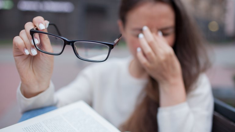 Eine Frau hat ihre Brille abgenommen und drückt die Finger gegen den Nasenrücken.