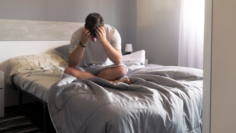 Man sieht einen Mann verzweifelt auf dem Bett sitzen