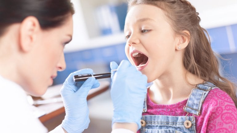 Eine Ärztin guckt einem Mädchen in den Mund.