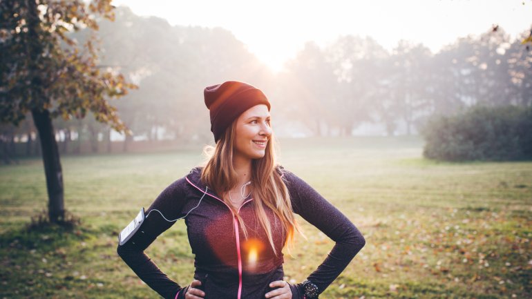 Das Bild zeigt eine junge Joggerin, die im Herbst vor einer Wiese steht.