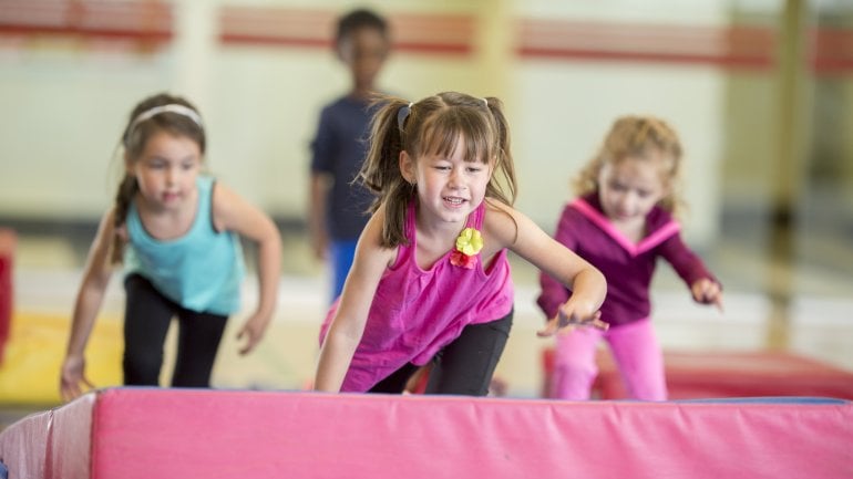 Drei Kinder toben über eine dicke Sportmatte.