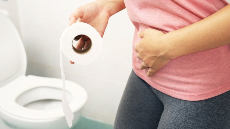 Eine Frau mit Stuhlinkontinenz steht vor der Toilette und hält Toilettenpapier in der Hand.