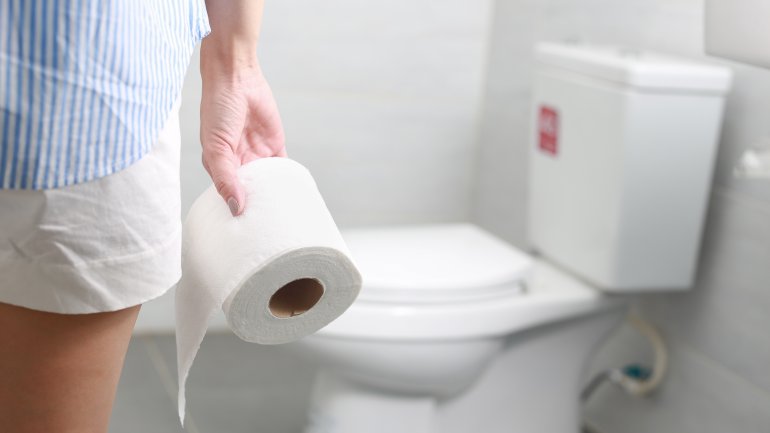 Eine Frau steht mit einer Rolle Klopapier vor einer Toilette