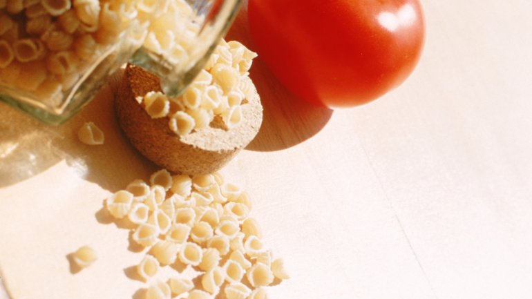 Das Bild zeigt eine Flasche mit Nudeln und eine Tomate.