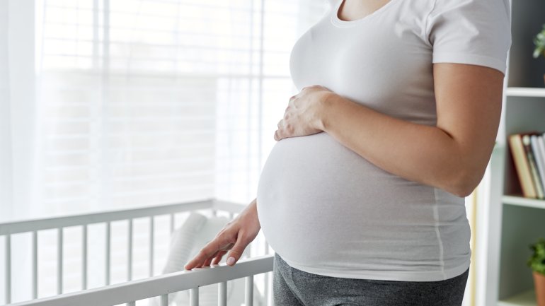 Eine hochschwangere Frau steht neben einem Babybett.