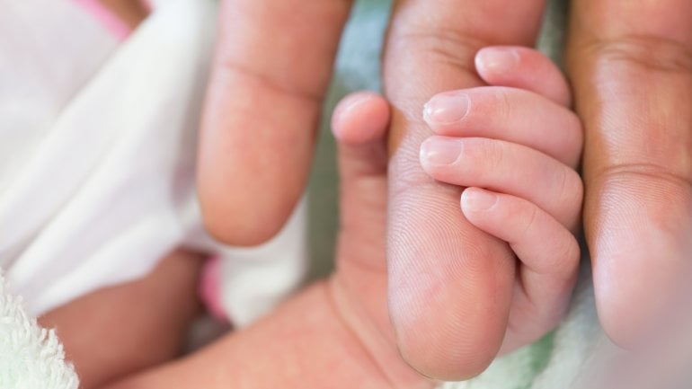 Man sieht die Hand eines Babys, die den Finger eines Erwachsenen umschließt.