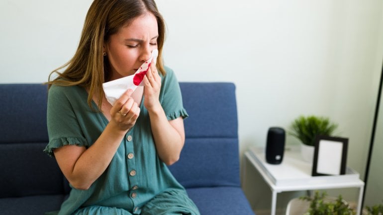 Frau mit Von-Willebrand-Syndrom sitzt auf Sofa und hat Nasenbluten.